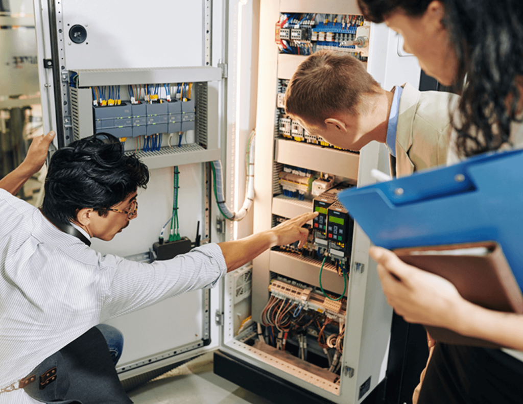 A team of technical experts collaborating on an industrial control panel inspection.