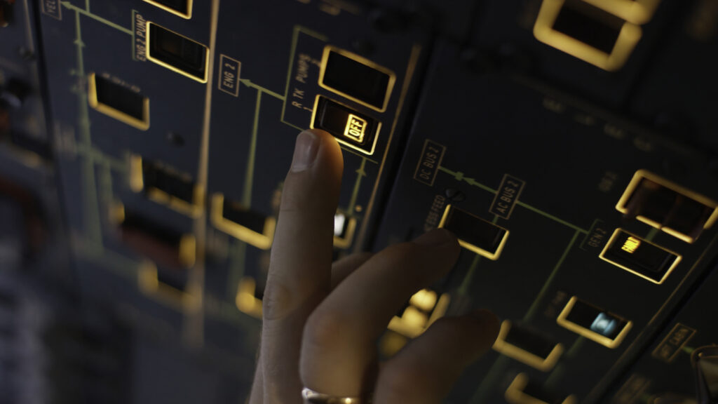 Close-up view of a hand interacting with a technical control board featuring various switches and amber indicator lights.
