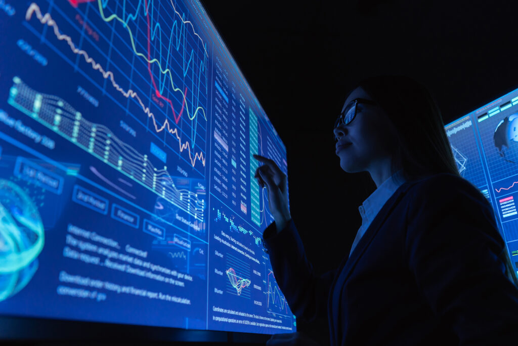 A data scientist analyzing complex visualizations and real-time metrics on a large digital dashboard.